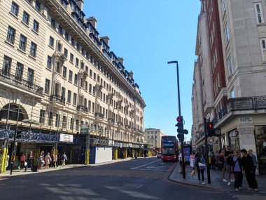 Londra, İngiltere - 17 Ağustos 2025: Yayalar Marylebone 'da açık mavi gökyüzü altında Chiltern Court da dahil olmak üzere tarihi binaların önünden geçerken Baker Caddesi boyunca klasik kırmızı çift katlı bir otobüs seyahat ediyor