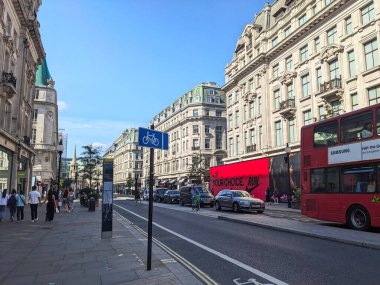 Londra, İngiltere - 09 Ağustos 2025: İkonik kırmızı çift katlı bir otobüs, temiz bir gökyüzü altında büyük bir West End alışveriş merkezi olan ünlü Regent Caddesi 'ndeki zarif tarihi mimari ve alışveriş merkezini geçti