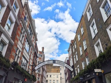Londra, İngiltere - 09 Ağustos 2025: Ünlü Carnaby Caddesi tabelası Soho 'daki popüler yayalara ait alışveriş alanının üzerinde asılı, tarihi binalar tarafından parçalı bulutlu bir gökyüzü altında çerçevelenmiş.