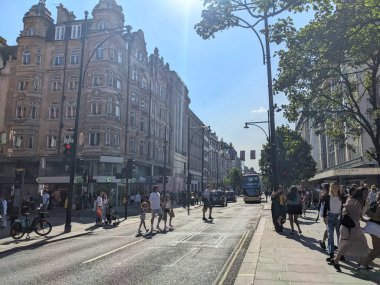 Londra, İngiltere - 09 Ağustos 2025: Kalabalık müşteriler ve yayalar güneşli bir yaz gününde arka planda klasik mimari ve Union Jack bayraklarıyla kalabalık Oxford Caddesi boyunca yürüyorlar