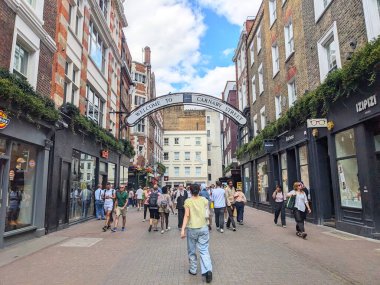 Londra, İngiltere - 09 Ağustos 2025: Alışverişçiler ve turistler, parlak bir yaz gününde, canlı ve tarihi Soho moda ve perakende bölgesinde Carnaby Caddesi tabelasına hoş geldiniz.