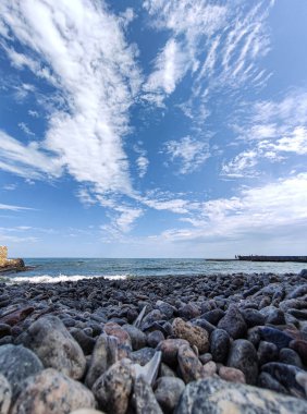 Bulutlardaki gökyüzü güneşli, denizdeki mavi gökyüzü, çakıl taşlı deniz.