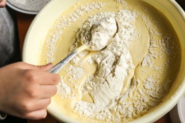 Koyu ahşap bir masada, sarı parmaklı bir çocuğun elleriyle mangır yapma süreci..