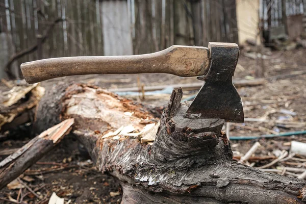 An axe with a wooden handle is stuck into a wooden stump.