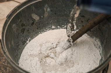 Kova koridorda yerde, içinde macun bir sopayla suyla karıştırılmış.