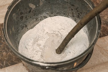 Kova koridorda yerde, içinde macun bir sopayla suyla karıştırılmış.