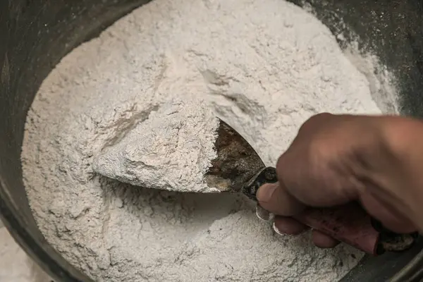 Bir kadının eli karıştırmak için macunu torbadan kovaya döker. Çalış ve dua et