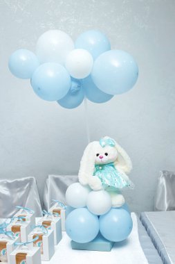 Mavi kalp şeklinde bir balon tutan yumuşak mavi pelüş bir tavşan, basit beyaz bir arka planda geçiyor.. 