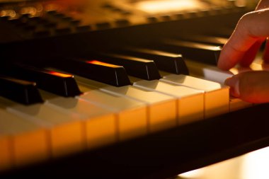 Aydınlatılmış piyano tuşları çalan, müzik, sanatçılık ve odaklanmış pratik yapan bir elin yakın çekimi.
