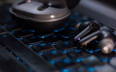 Kablosuz kulaklıklar ve şarj çantası mavi bir dizüstü bilgisayarın klavyesinde duruyor. Teknoloji kavramı, uzak çalışma, modern yaşam tarzı ve eğlence..