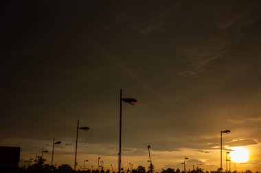 Sokak lambaları ve ağaçların gölgesi altın bir günbatımı gökyüzüne karşı. Şehir manzarası ve akşam manzarası kavramı