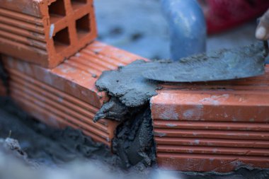 Duvarın inşaatı sırasında kırmızı tuğlaya ıslak çimento harcı döken bir malanın makro çekimi. Tuğla döşeme süreci ve duvarcılık araçlarının özgün bir görüntüsü.