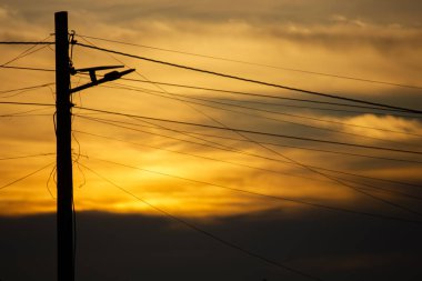 Elektrik direğinin silueti ve elektrik kabloları altın bir günbatımı gökyüzüne karşı. Asya 'da şehir manzarası.