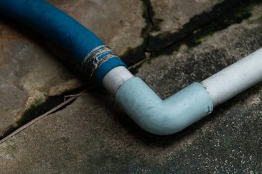 Çatlak beton zemine bağlı mavi ve beyaz PVC borular. Onarım ve bağlantı kavramı.