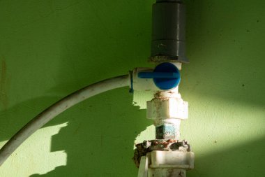 Eski PVC borulardan oluşan bir ağ ve canlı yeşil bir duvarda bir vana. Ev onarımı ve mimari kavramı