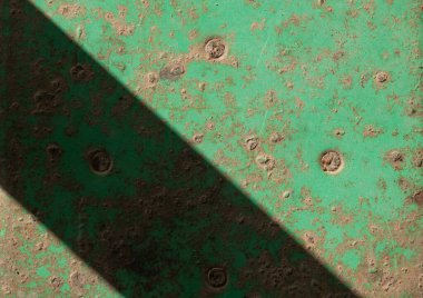 Keskin çapraz gölgesi olan paslı, yeşil bir metal yüzey. Çürüme ve ışığın soyut arkaplanı.