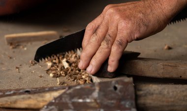 Bir marangozun elinin bir atölyede tahta testeresini keserken yakın plan çekimi. El işi ve marangozluk konsepti