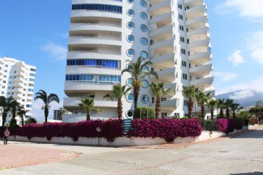 Türkiye 'de Alanya' nın güzel caddeleri. Çiçekler, ağaçlar, yelkenli şeklinde bir apartman binası ve Türkiye sokaklarında tekne şeklinde bir kütük. Temiz bulutsuz gökyüzü
