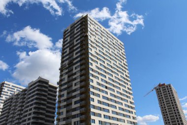 Şehirdeki modern binalar, yeni yüksek binaların ön cepheleri ve mavi gökyüzü arka planına karşı vinçleri olan inşaat alanları.