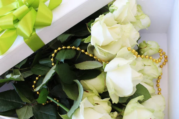 white roses and a white gift box with gold and light green ribbon on a white background with space for your text.