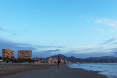 Adam plajda koşuyor. İspanya 'da Alicante şehri ve deniz üzerinde gün doğumu.