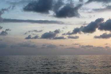 Gün batımında okyanusta bulutlu bir tekne.