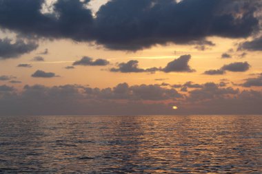 Okyanusun üzerinde bir gün batımı ve suda bir tekne.