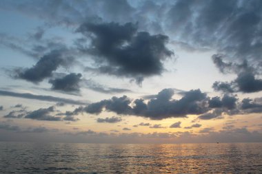 Gün batımında okyanusta bulutlu bir tekne.