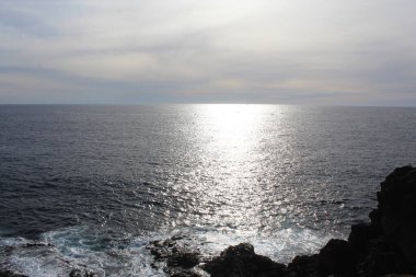 Kayaların ve okyanusların üzerinde güneş parlayan doğal mavi bir arka plan.