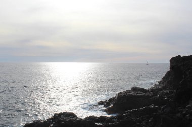 Kayaların ve okyanusların üzerinde güneş parlayan doğal mavi bir arka plan.