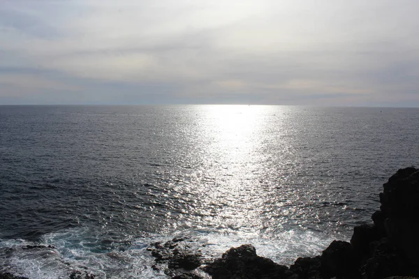 Kayaların ve okyanusların üzerinde güneş parlayan doğal mavi bir arka plan.