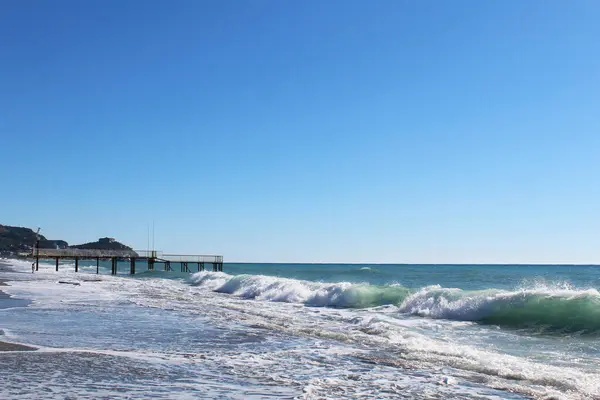 view of the mediterranean sea in the morning. clear blue sky over the sea. big waves with white foam crashing on beach and sea pier in mediterranean sea