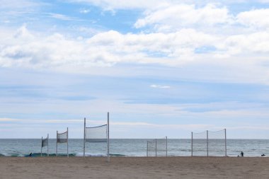 Plajda voleybol ağı, deniz üzerinde mavi gökyüzü olan kumlu sahilin güzel bir manzarası.