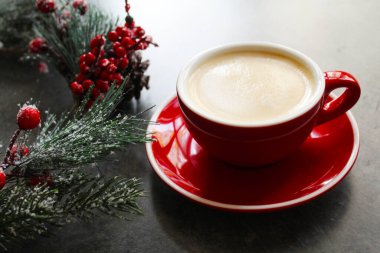 Gri ahşap bir masada kırmızı bir fincanda kahve ve Noel süsü.