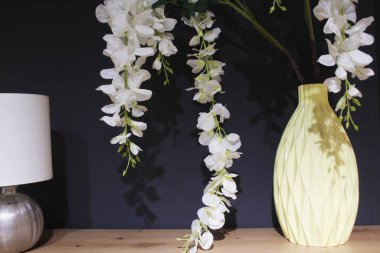 Beyaz odada orkide, odanın içinde çiçekler olan bir vazo.