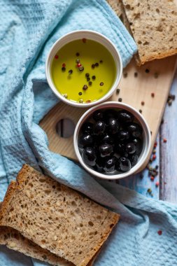 Mavi bir mutfak havlusunun üzerinde siyah zeytinler bir kase zeytinyağı ve bir parça siyah ekmek var. Yüksek kalite fotoğraf