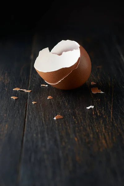 brown egg shell broken or crack with pieces scattered on the surface, isolated on rustic black table top surface with blurry background, selective focus with copy space