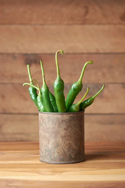 green chillies in an old rusty cup or container, common vegetable used for their spicy taste, placed on wooden table top with copy space