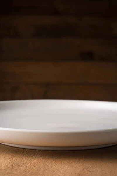 空白的白色盘子放在木制桌子顶部 与深色模糊的木制背景 食物摄影背景或背景相对照 在浅浅的视野中近距离侧视 带有复制空间 — 图库照片