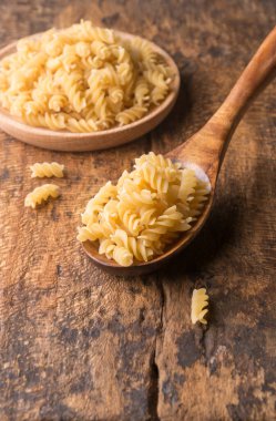 Tahta bir kaşıkta pişmemiş makarnanın çeşitli çeşitleri, ahşap arka plan, diyet ve gıda konsepti, fotokopi alanı ile sığ alan derinliğinde çekilir.