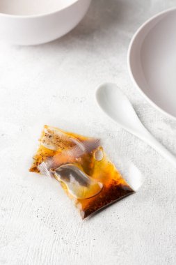 Hazır palmiye yağı paketleri soğan ve kırmızı biber tozu ile birlikte, beyaz masa üstünde hazır erişte için yağda kızartma olarak kullanılır, boş tabak ve fincanla yumuşak odaklı arka plan