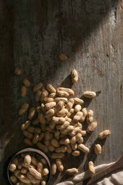 Yerfıstığı, yer fıstığı, pindar ya da maymun fındığı olarak da bilinen eski bir fincanla ahşap arka planda soyulmamış yer fıstığı yığını.