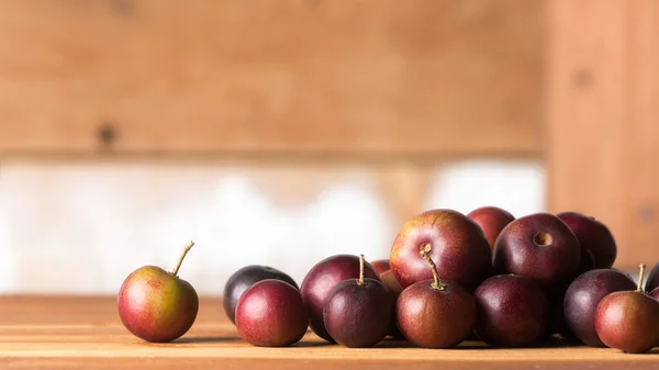 close-up of governor\'s plum fruits on wooden table top, flacourtia indica, also known as ramontchi, madagascar plum or indian plum, reddish black fleshy fruits, soft-focus wooden background
