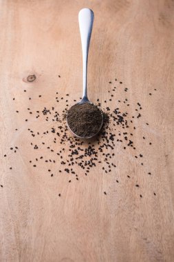 Siyah kimyon, kimyon ya da kalonji olarak da bilinen toz ve kavrulmuş siyah tohumlar, bir kaşık içinde, bir masanın üstüne serpilmiş tohumlar, fotokopi alanı ile sığ alan derinliği