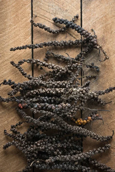 dried black peppercorns, dry black pepper fruits or drupes on a wooden table top, spicy and seasoning ingredient, taken straight from above