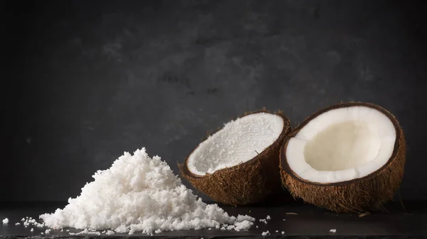 stock image pile of scraped or desiccated coconut with two half coconut shell, healthy tropical fruits on a black surface, dark textured background with copy space