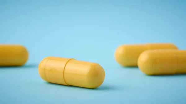 close-up of yellow gelatin capsules pills, oral medical drug filled with powder or liquid form on blue background, selective focus with copy space, complementary color theme