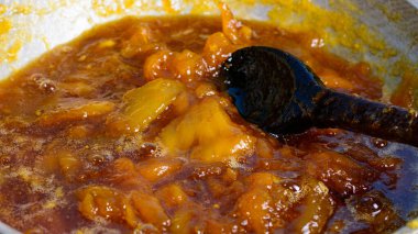 Mango reçeli yapmak, şeker şuruplu mango parçaları kaynatmak, karıştırma kaşıklı ev yapımı tatlı yiyecekler, yakın çekim.