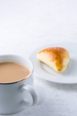 Beyaz desenli arka planda şekerli çörek ve bir fincan sütlü çay