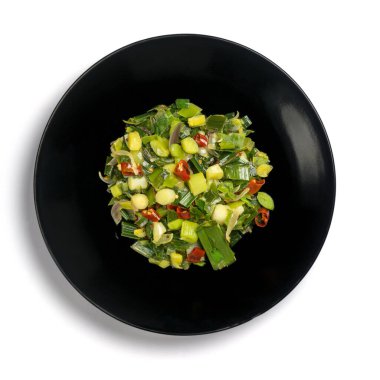 Kırmızı biberli ve soğanlı kızarmış pırasa, siyah tabakta yeşil vejetaryen yemeği, beyaz arka planda izole edilmiş, yukarıdan alınmış.